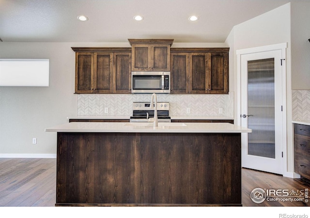 kitchen featuring an island with sink, appliances with stainless steel finishes, hardwood / wood-style floors, and dark brown cabinetry