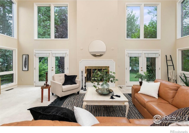 carpeted living room with french doors, a brick fireplace, and a high ceiling