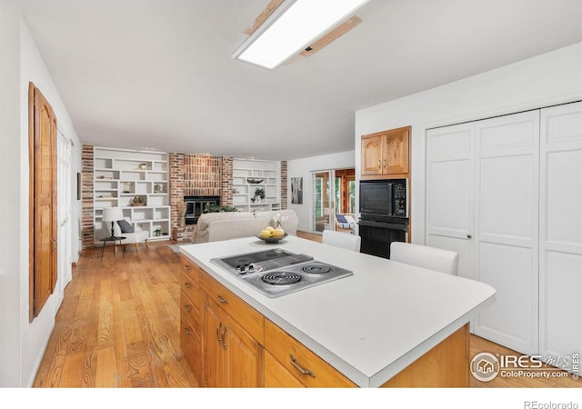 kitchen featuring a center island, light hardwood / wood-style floors, a brick fireplace, and black appliances