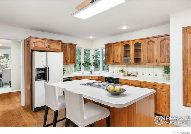 kitchen with a breakfast bar, tasteful backsplash, light hardwood / wood-style flooring, a kitchen island, and white refrigerator with ice dispenser