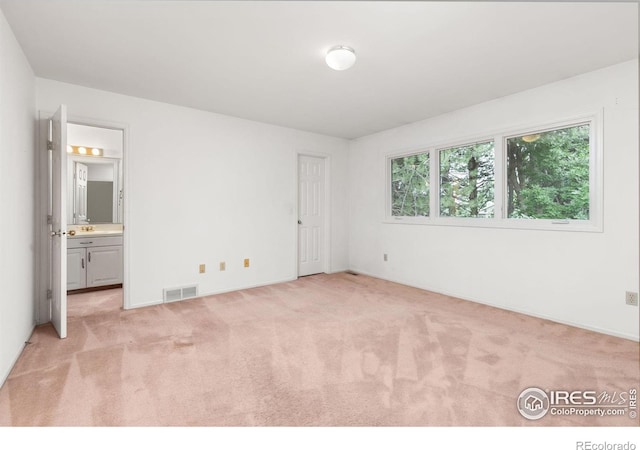 unfurnished bedroom with ensuite bathroom and light colored carpet