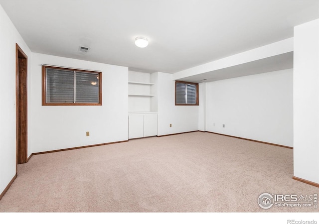 spare room featuring built in shelves and light colored carpet