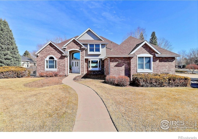 view of front of house with a front yard, brick siding, and roof with shingles