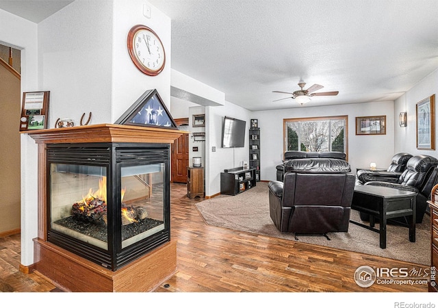 living room featuring hardwood / wood-style flooring, a multi sided fireplace, ceiling fan, and a textured ceiling