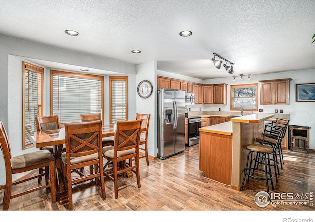 kitchen with rail lighting, sink, light wood-type flooring, appliances with stainless steel finishes, and a kitchen breakfast bar