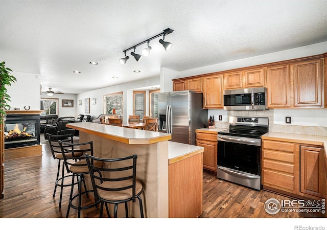 kitchen with a breakfast bar area, appliances with stainless steel finishes, a multi sided fireplace, a kitchen island, and dark hardwood / wood-style flooring