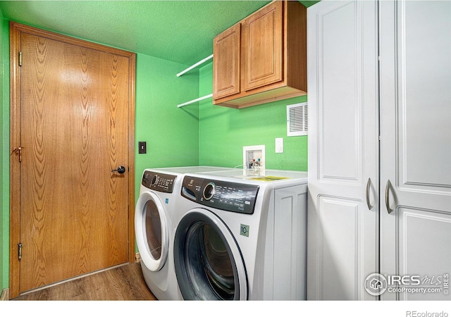 laundry area with cabinets, washing machine and clothes dryer, wood-type flooring, and a textured ceiling