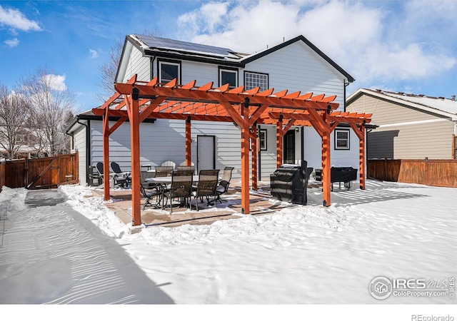 snow covered rear of property with a pergola and solar panels