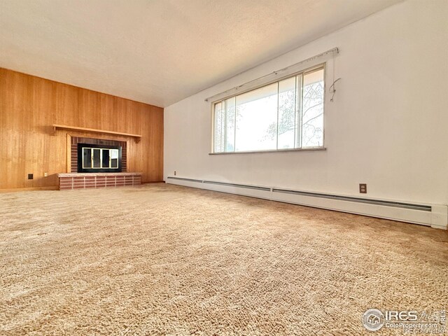 unfurnished living room featuring a brick fireplace, wooden walls, a baseboard radiator, and carpet