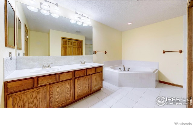 bathroom featuring tasteful backsplash, tile patterned flooring, vanity, tiled tub, and a textured ceiling