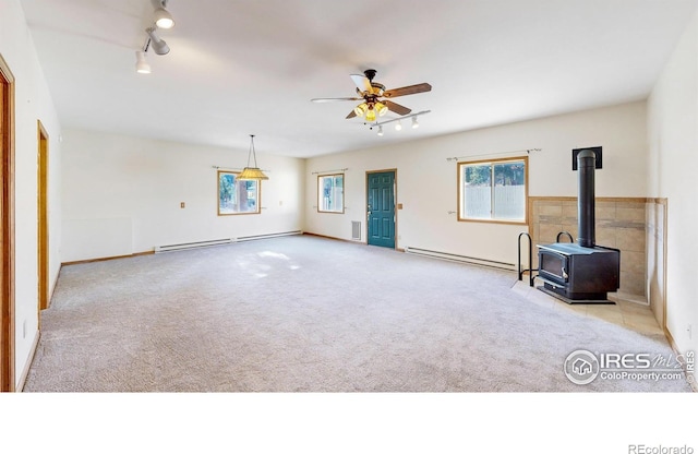 unfurnished living room with light carpet, a baseboard heating unit, track lighting, and a wood stove