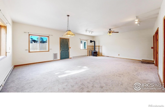 unfurnished living room featuring carpet flooring, a baseboard heating unit, rail lighting, and a wood stove