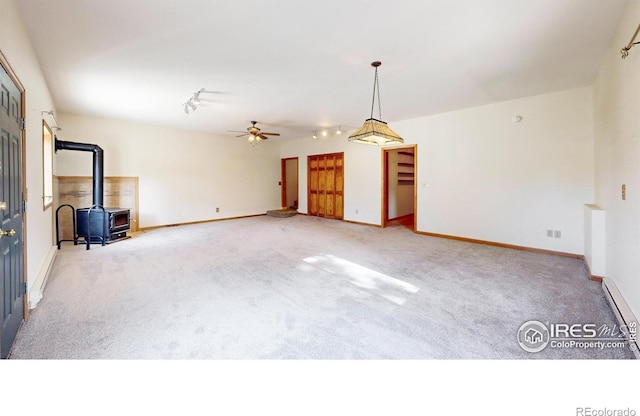 unfurnished living room with ceiling fan, a baseboard radiator, carpet floors, and a wood stove