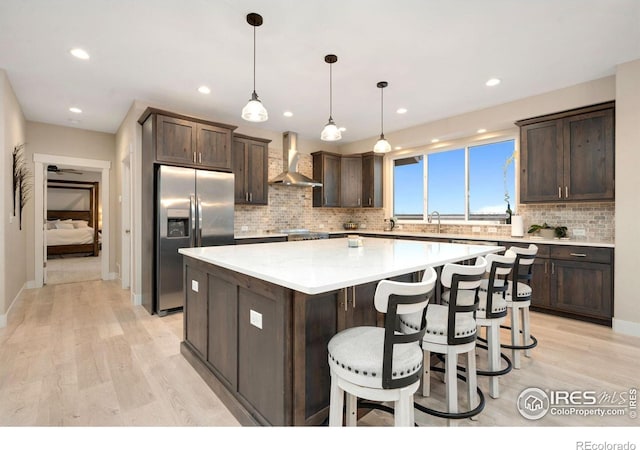 kitchen with a center island, stainless steel fridge, pendant lighting, light hardwood / wood-style floors, and wall chimney range hood