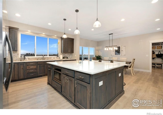 kitchen featuring hanging light fixtures, dark brown cabinets, stainless steel refrigerator, and a kitchen island