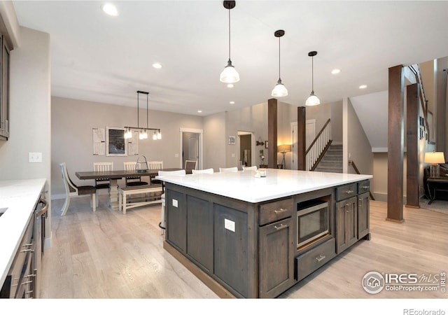 kitchen featuring stainless steel microwave, dark brown cabinetry, decorative light fixtures, and a kitchen island