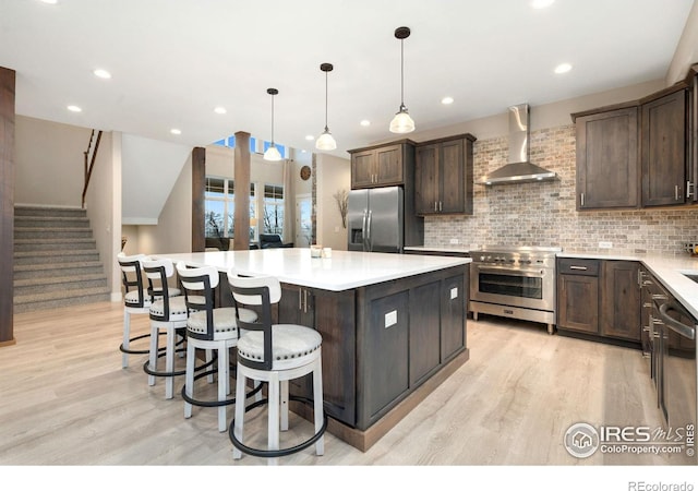 kitchen with hanging light fixtures, stainless steel appliances, tasteful backsplash, a kitchen island, and wall chimney exhaust hood