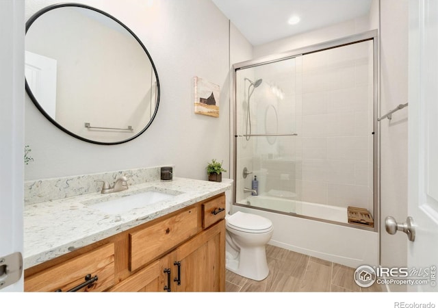 full bathroom with vanity, hardwood / wood-style flooring, shower / bath combination with glass door, and toilet