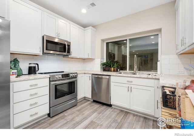 kitchen featuring sink, light stone counters, appliances with stainless steel finishes, light hardwood / wood-style floors, and white cabinets