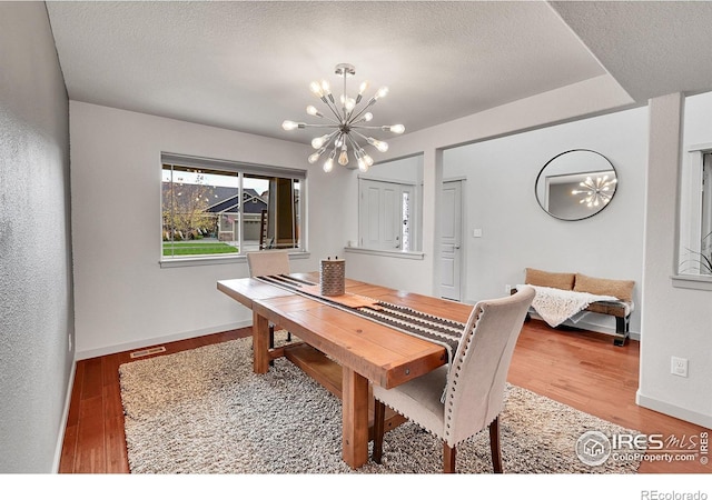 dining area featuring wood-type flooring, a textured ceiling, and an inviting chandelier