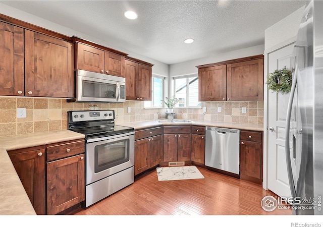 kitchen with sink, stainless steel appliances, light hardwood / wood-style floors, a textured ceiling, and decorative backsplash