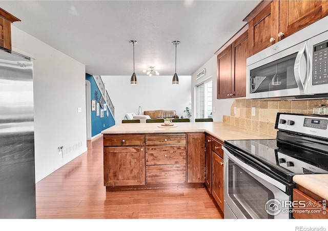 kitchen featuring hanging light fixtures, stainless steel appliances, tasteful backsplash, light hardwood / wood-style floors, and kitchen peninsula