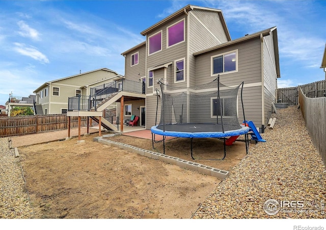 rear view of property featuring a wooden deck, a trampoline, and a patio area