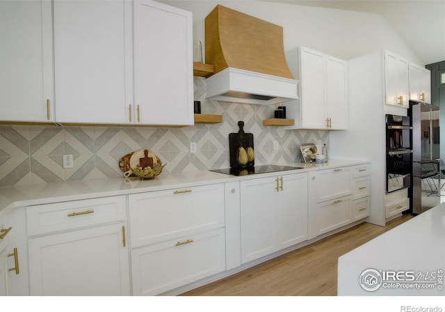 kitchen featuring white cabinetry, backsplash, black appliances, and premium range hood