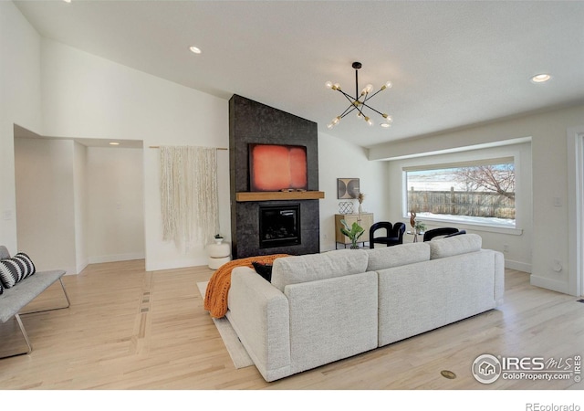 living room featuring a tiled fireplace, lofted ceiling, a notable chandelier, and light hardwood / wood-style floors