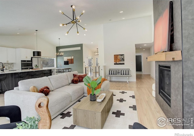 living room with a large fireplace, high vaulted ceiling, a notable chandelier, and light wood-type flooring