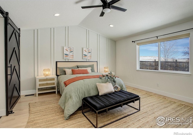 bedroom with a barn door, light wood-type flooring, lofted ceiling, and ceiling fan