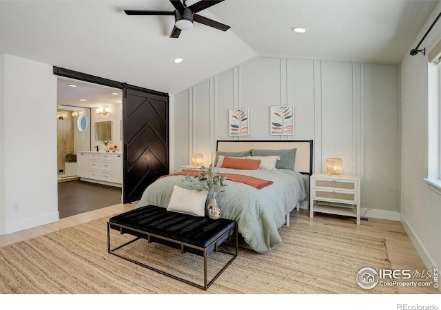 bedroom with wood-type flooring, a barn door, lofted ceiling, and ceiling fan