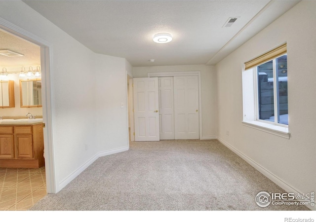 unfurnished bedroom featuring light carpet, a closet, a textured ceiling, and ensuite bathroom