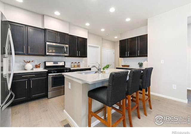 kitchen featuring a kitchen bar, sink, a center island with sink, appliances with stainless steel finishes, and light hardwood / wood-style floors