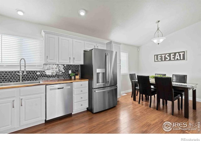 kitchen with pendant lighting, butcher block countertops, white cabinetry, sink, and stainless steel appliances