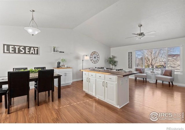 kitchen featuring vaulted ceiling, a kitchen island, white cabinets, hanging light fixtures, and light wood-type flooring