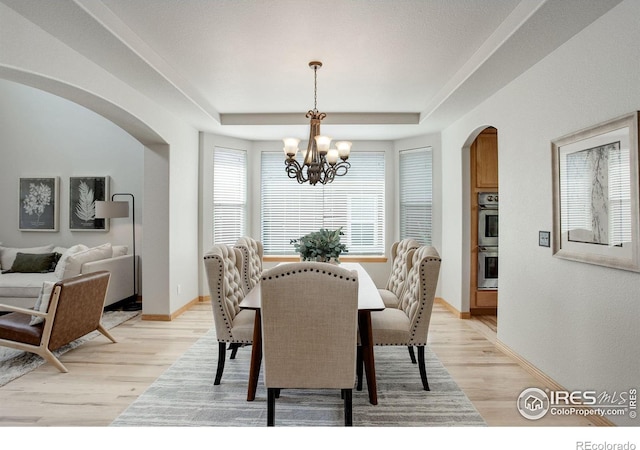 dining area with an inviting chandelier, a tray ceiling, and light hardwood / wood-style flooring