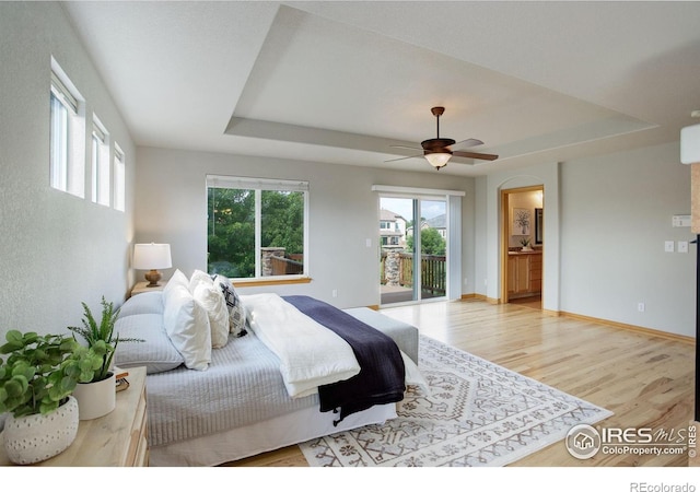 bedroom featuring multiple windows, access to exterior, a tray ceiling, and ceiling fan