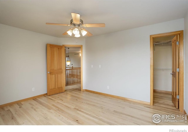 unfurnished bedroom with a spacious closet, a closet, ceiling fan, and light wood-type flooring