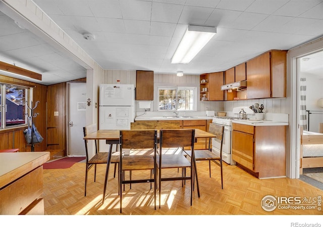 kitchen featuring white appliances, light parquet floors, and wood walls