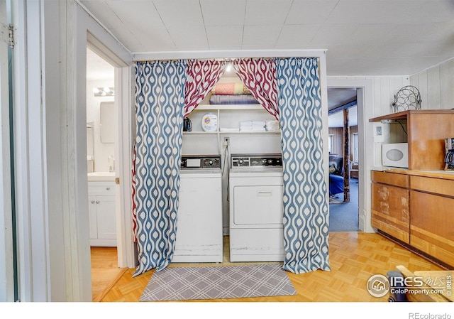 clothes washing area featuring sink, washing machine and dryer, and light parquet floors