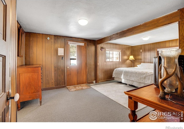 carpeted bedroom with beamed ceiling, wooden walls, and a textured ceiling