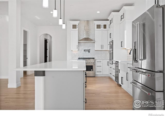 kitchen with white cabinets, high quality appliances, a kitchen island, and wall chimney range hood