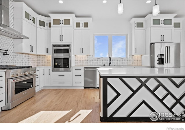 kitchen with high quality appliances, wall chimney range hood, pendant lighting, and white cabinets