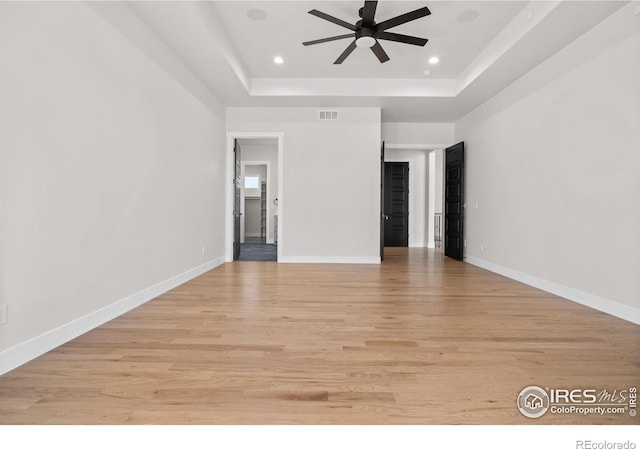 empty room featuring a tray ceiling, light hardwood / wood-style flooring, and ceiling fan