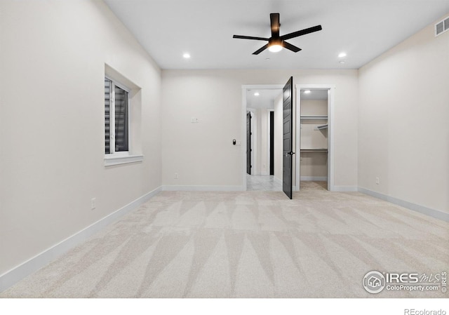 unfurnished bedroom with light carpet, a walk in closet, a closet, and ceiling fan