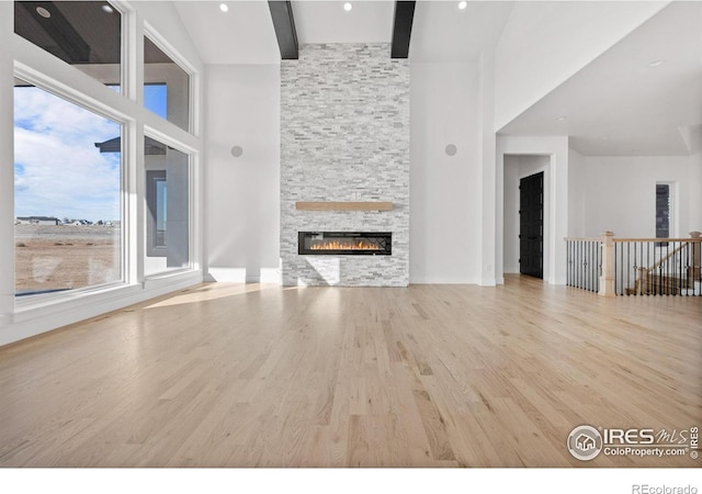 unfurnished living room featuring light hardwood / wood-style flooring, a fireplace, high vaulted ceiling, and beamed ceiling