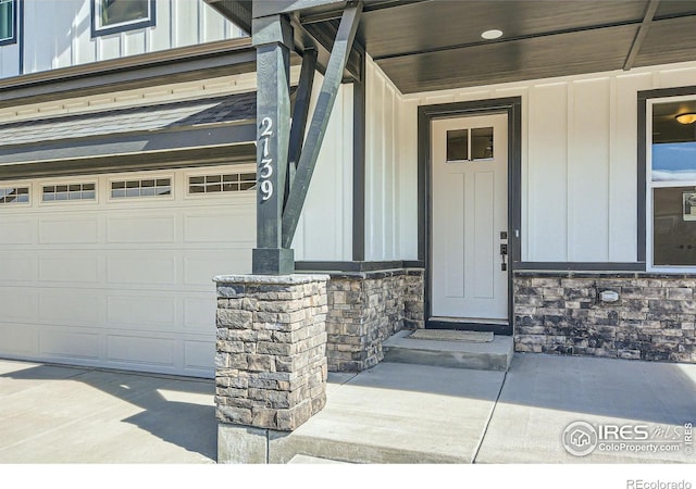 doorway to property with board and batten siding, a porch, a garage, and stone siding