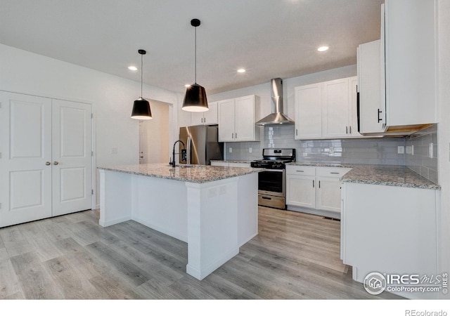 kitchen featuring white cabinetry, a center island with sink, appliances with stainless steel finishes, decorative backsplash, and wall chimney range hood