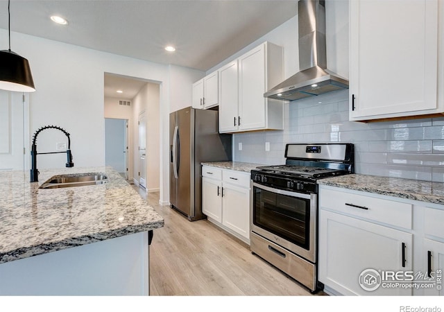 kitchen with wall chimney range hood, sink, hanging light fixtures, stainless steel appliances, and white cabinets